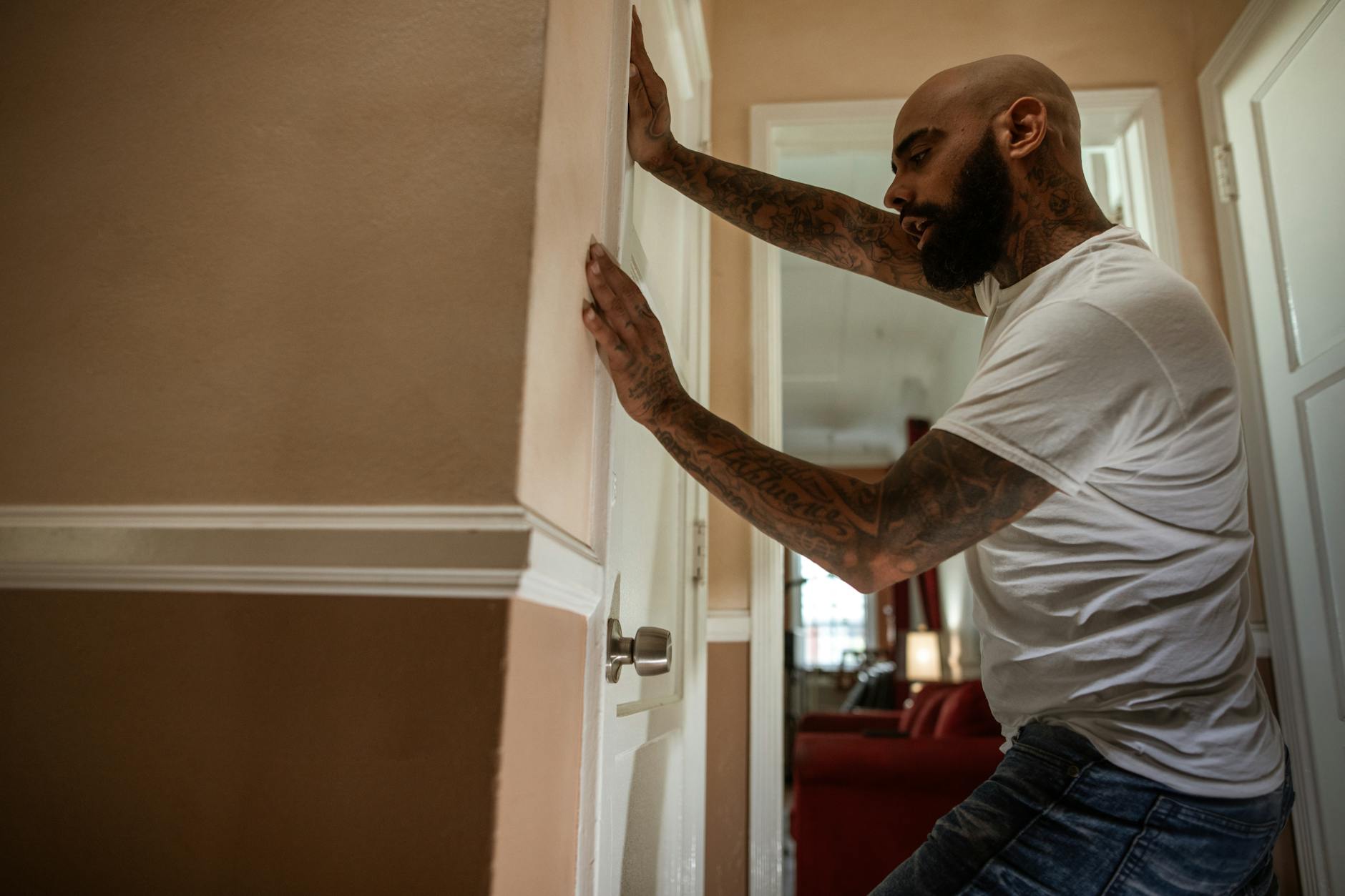 man in white t shirt and blue denim jeans standing near white wooden door